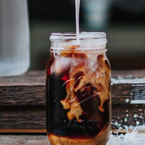 Cold brew coffee in a mason jar, milk being poured on top of it and a little bit of splashing